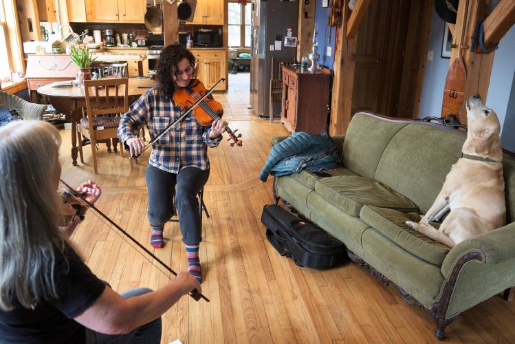 Fiddle teacher Beth Telford, left, plays a tune with student Lauren Bomalaski, of Tunbridge, right, as her yellow Lab Trouble stretches on the couch in Braintree, Vt., on Wednesday, March 6, 2024. Telford encourages her students to learn the classical bow and violin holds to help avoid repetitive stress injuries. (Valley News - James M. Patterson) Copyright Valley News. May not be reprinted or used online without permission. Send requests to permission@vnews.com.