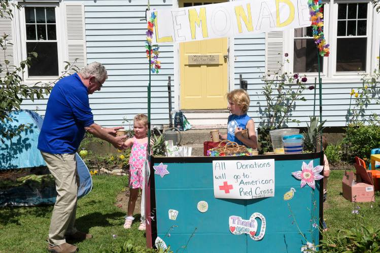 Delilah Templeton, 5, middle, hands a cup of lemonade to Steve Hinkley, of Claremont, as Ashton White, 8, right, prepares a cup for Hinkley's wife Ellen in Claremont, N.H., on Tuesday, August 22, 2023, during a lemonade stand fundraiser for the Hawaiian Red Cross in the aftermath of the deadly wildfires that destroyed the town of Lahaina on Maui. Leah Couture, White's mother, held the fundraiser outside her home childcare business at the encouragement of her neighbor Janette Coombs. (Valley News - James M. Patterson) Copyright Valley News. May not be reprinted or used online without permission. Send requests to permission@vnews.com.