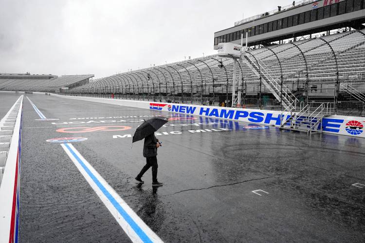 John Basher, of Buffalo, N.Y., carries an umbrella while walking on the rain-soaked race track, Sunday, July 16, 2023, at New Hampshire Motor Speedway, in Loudon, N.H. Sunday's Crayon 301 NASCAR Cup Series race has been postponed until Monday, July 17, 2023, due to inclement weather, officials said Sunday. (AP Photo/Steven Senne)