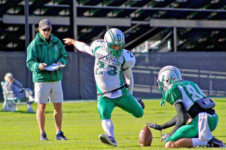 Dartmouth College football place kicker Foley Schmidt practices under the gaze and stopwatch of head coach Buddy Teevens. The holder is Michael Reilly and Big Green super fan Winnie Stearns is on the far left.