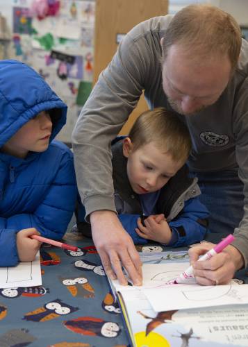 John Crossley, right, helps his sons Casper, 4, center, and Hector, 7, draw dinosaurs that start with the first letter of their names during story time at the Hartland Public Library in Hartland, Vt., on Saturday, Jan. 20, 2024. The theme of the week for story time was the alphabet, and participants decorated letters after reading alphabet books. (Valley News / Report For America - Alex Driehaus) Copyright Valley News. May not be reprinted or used online without permission. Send requests to permission@vnews.com.