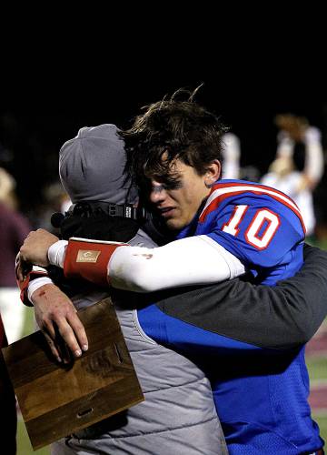 As Burr & Burton celebrates their Division I state championship victory across the field, Hartford quarterback Brayden Trombly holds the runner-up plaque and hugs his father and head coach Matt Trombly in Rutland, Vt., on Nov. 11, 2023. The senior co-captain is three-year starter on the team, who lost 35-28 in the final. (Valley News - Geoff Hansen) Copyright Valley News. May not be reprinted or used online without permission. Send requests to permission@vnews.com.