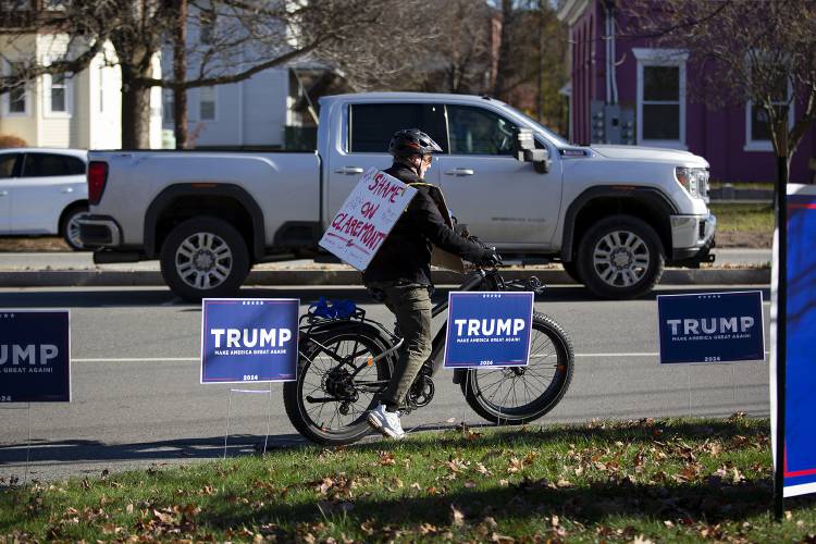 A cyclist wears a sign that says “Shame on Claremont for welcoming such a pervert” as he rides past the entrance of a campaign rally for former President Donald Trump at Stevens High School in Claremont, N.H., on Saturday, Nov. 11, 2023. (Valley News / Report For America - Alex Driehaus) Copyright Valley News. May not be reprinted or used online without permission. Send requests to permission@vnews.com.