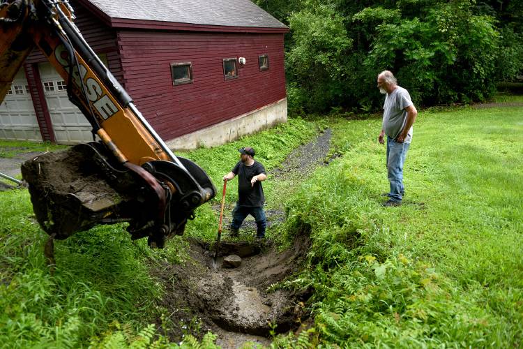 Evan McClure of the Hartland (Vt.) Highway Department hand-digs debris and mud from a culvert while BJ Mattson, also of the Highway Department, takes materials out with an excavator on Monday, July 24, 2023, in Hartland. Steve Allen, the homeowner, is on the right. Allen lost his driveway after heavy rains hit on Friday. Sections of Jenneville Road, where Allen lives, were impassable due to the rain. (Valley News - Jennifer Hauck) Copyright Valley News. May not be reprinted or used online without permission. Send requests to permission@vnews.com.
