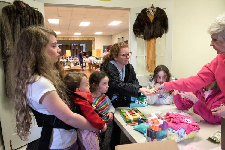 Donna Ron, center, takes her change from Sherry Pressey, right, after shopping for a bag of treasures with her daughters, from left, Anna, 12, baby Shira, Naomi, 6, and Abigail Ron, 9, at the Etna Ladies Aid spring rummage sale at Trumbull Hall in Etna, N.H., on Friday, April 12, 2024. The organization donates all proceeds from its spring and fall sales to local organizations and projects, and they will be adding an August auction to their fundraisers this year. (Valley News - James M. Patterson) Copyright Valley News. May not be reprinted or used online without permission. Send requests to permission@vnews.com.