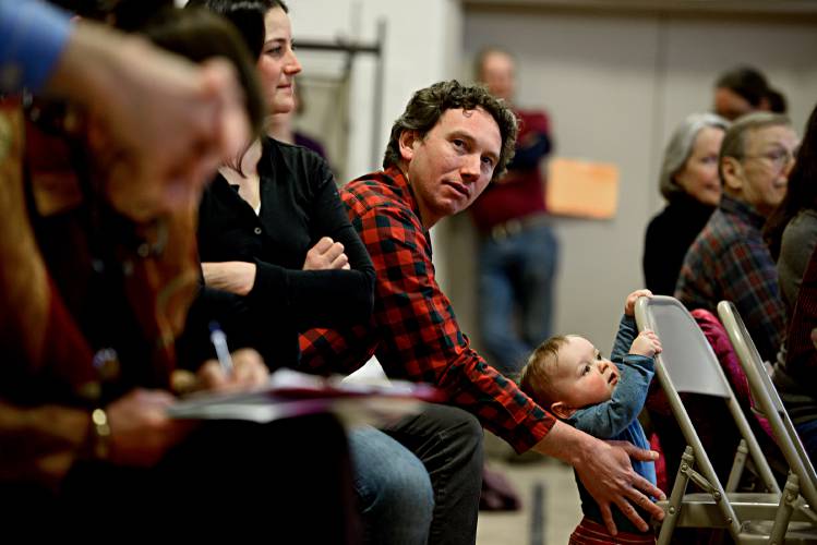 Will Davis, of Sharon, Vt., steadies his son Tal, 9 months during Sharon's Town Meeting on March 6, 2018. His wife Stephanie Davis sits with them on the left. (Valley News - Jennifer Hauck) Copyright Valley News. May not be reprinted or used online without permission. Send requests to permission@vnews.com.