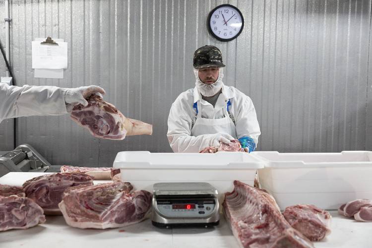 Zach Maguira, left, tosses a cut of pork into a bin on a table in front of Dan Gagnon as they work on an order at Granite State Packing in Claremont, N.H., on Tuesday, July 18, 2023. The packing co-op opened in March after purchasing a meat processing facility that had been empty for several years. (Valley News / Report For America - Alex Driehaus) Copyright Valley News. May not be reprinted or used online without permission. Send requests to permission@vnews.com.